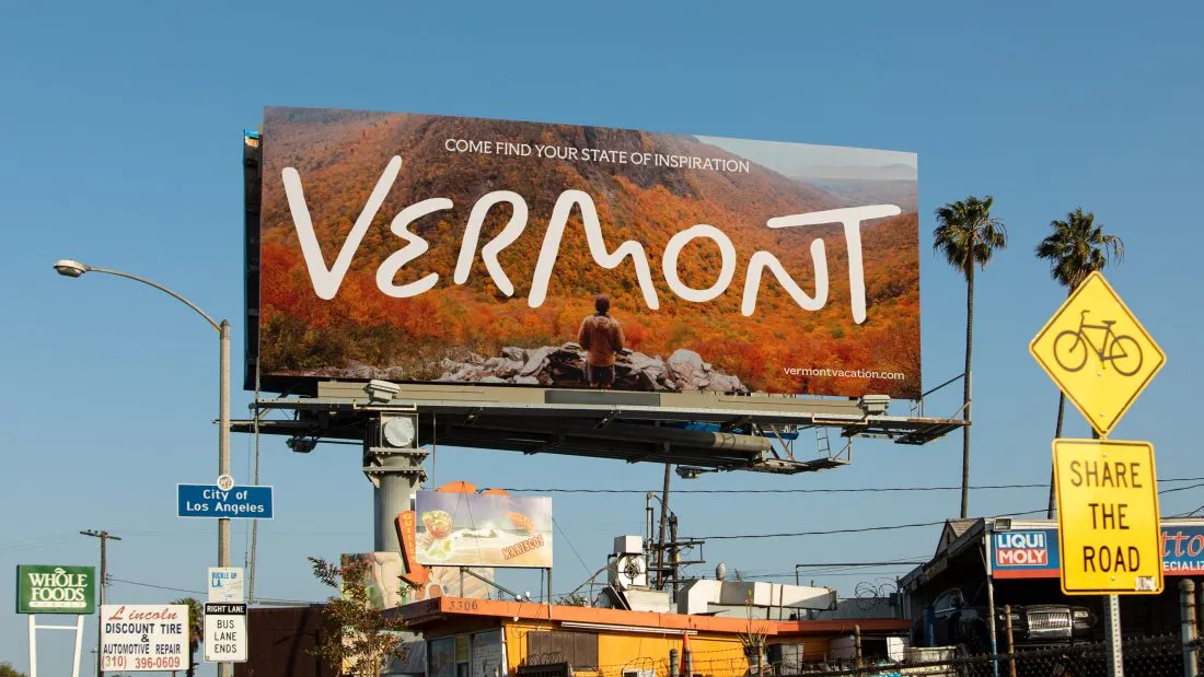 Valla publicitaria en Los Ángeles con el nuevo wordmark de Vermont hecho a mano sobre una fotografía de montañas con follaje otoñal y la línea "Come find your state of inspiration".